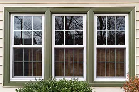 set of 3 vinyl windows with green trim and beige siding
